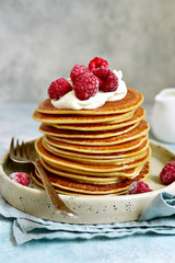 Stack of homemade delicious hot pancakes with honey, cream and raspberry.