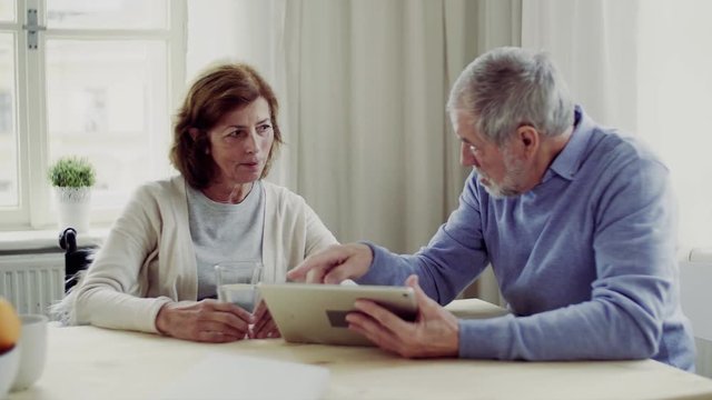 Senior couple with wheelchair and tablet sitting at the table at home, talking.