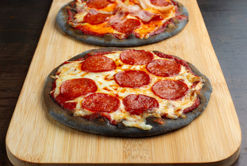 Creative pizza on black dough, two pieces on the board.