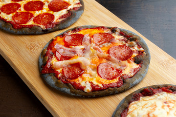 Creative pizza on black dough, three pieces on the board.