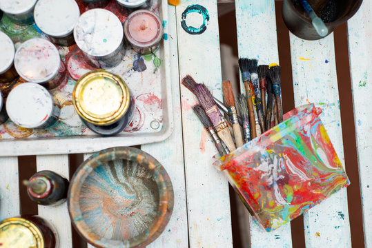 Paint brushes on technique ebru lie on a white wooden table near the cans of paint