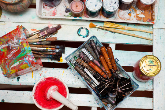 Paint brushes on technique ebru lie on a white wooden table near the cans of paint