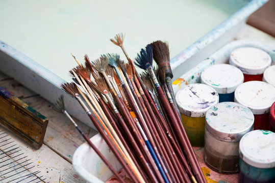 Paint brushes on technique ebru lie on a white wooden table near the cans of paint