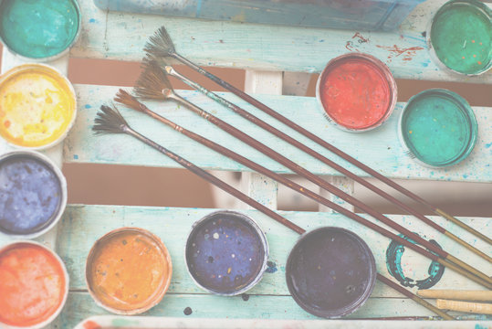 Ebru paint brushes lay on a white wooden table against a background of paint covers