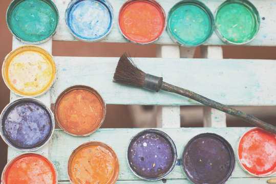 Ebru paint brushes lay on a white wooden table against a background of paint covers