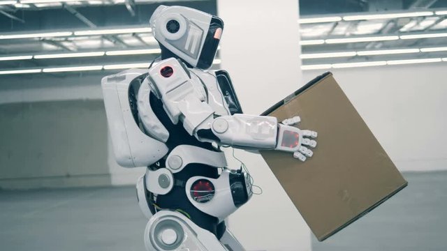 Human-like robot is lifting a box and carrying it
