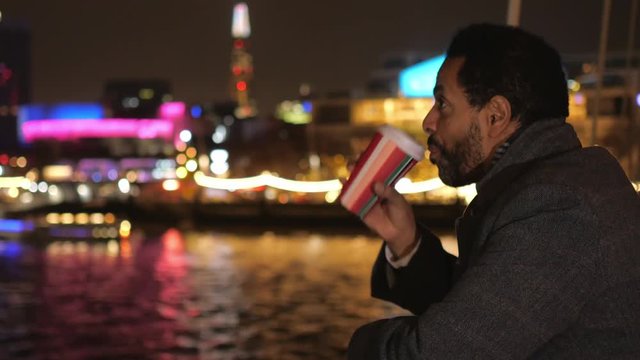 Man drinks coffee on a bridge in London and enjoys the city lights at night