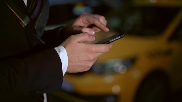 Close up shot of male hand with a phone. Taxi on the bakcground