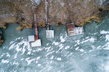 Aerial view of winter frozen lake with wooden houses on pier