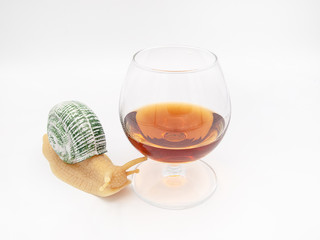 Glass of cognac, whiskey or rum with a decorative snail isolated on a white background, as a concept of alcohol drinking effects on the human body