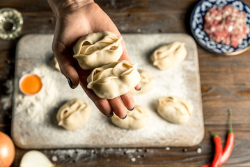 Uzbek national food manta, like dumplings, on a wooden board, lie in flour with an egg. Hand holds manta