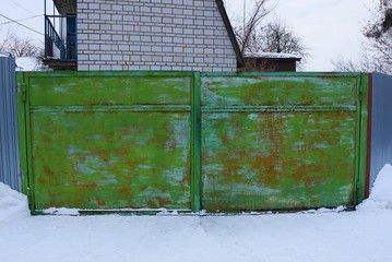 old green rusty metal gate on a street in white snow