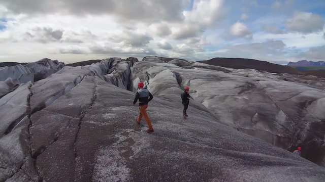 Aerial, orbit, drone shot. following a man, walking on huge ice blocks, on a cloudy, summer day, in Iceland