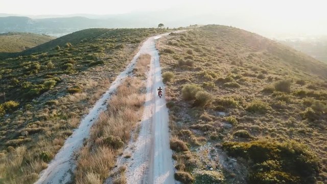 Aerial shot of following a motorcyclist while he drives on a gravel road during golden hour on a mountain next to Athens, Greece