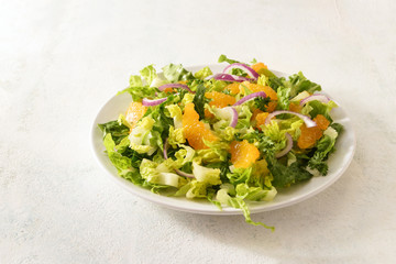 healthy salad from tangerines and lettuce with red onions on a white plate, bright background with large copy space