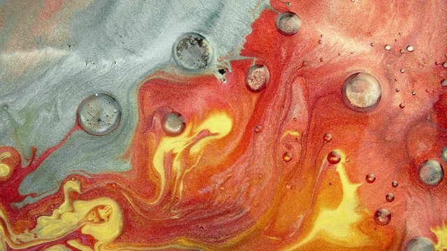 Colorful sparkling paints mix in beautiful patterns. Oil ink of yellow, orange, grey and other colors spread on the surface and mix one into another creating amazing textures and design.