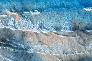 Fototapeta na wymiar Aerial view of a transparent blue sea with beautiful waves at sunny evening in summer. Tropical aerial landscape with ocean with azure water, sandy bottom at sunset. Top view from drone. Nature
