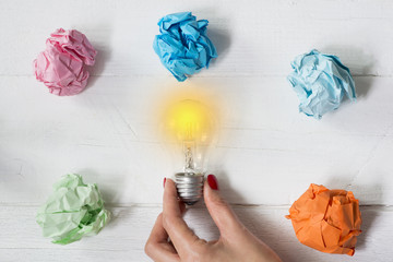 Brilliant and original idea suggested by glowing light bulb in woman’s hand and crumpled paper against white background