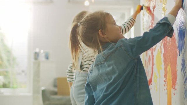 Two Happy Little Girls with Hands Dipped in Colorful Paint Put Handprints and Draw on the Wall