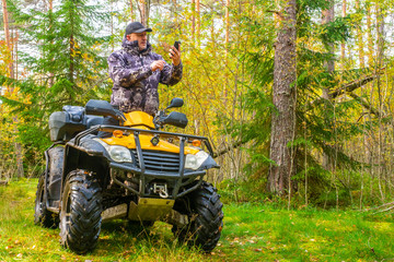 Fototapeta premium ATV. A man rides through the forest on an all-terrain vehicle. Quad bike. In the woods. Trip to the forest on ATV. The traveler checks the route on the map on the phone.