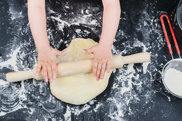 child hands making the dough with flour, rolling pin and wheat ears on rustic wooden table top view. Homemade pastry for bread or pizza. Bakery background. 