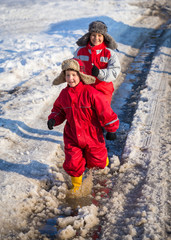 Two kids in rainboots running on the ice puddle