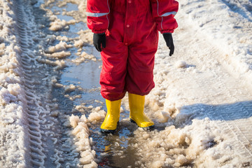 Kid legs in rainboots standing in the ice puddle