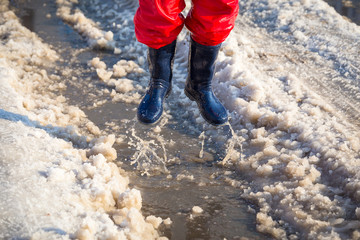 Kid in rainboots jumping in the ice puddle