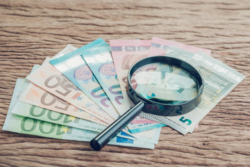 Finance saving, tax, investment or searching for yield concept, magnifier glass on pile of Euro banknotes on wooden table, European Union government economics situation