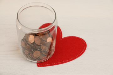 Red heart and donation jar with coins on light background