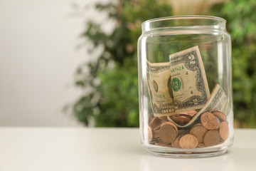 Donation jar with money on table against blurred background. Space for text