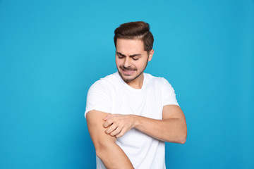 Young man scratching arm on color background. Annoying itch