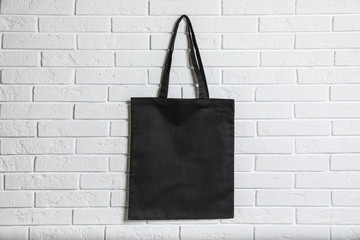 Eco tote bag hanging on white brick wall. Space for design