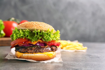 Tasty burger with bacon on grey table. Space for text