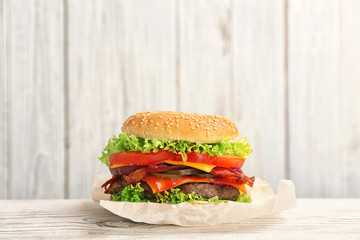 Tasty burger with bacon on table against wooden background. Space for text