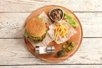 Board with tasty burger, french fries and vegetables on wooden table, top view