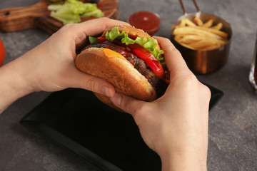 Woman holding tasty burger with bacon over grey table, closeup