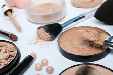 Composition with skin foundation, powder and beauty accessories on white background