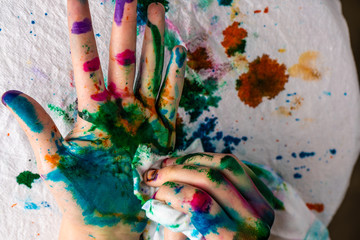  A child cleans up hands that are covered in red, pink, yellow, orange, red, blue, green, and purple ink.  Concepts: art, education, play, watercolor, finger painting, mess, creativity, fun, enjoyment