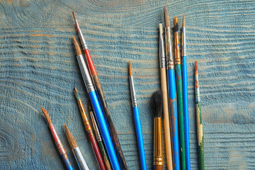 Different paint brushes on wooden background, top view