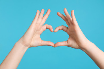Young woman making heart with her hands on color background, closeup