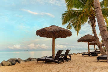 Zen scene of chaise lounge chairs on beach with thatched umbrellas and calm ocean