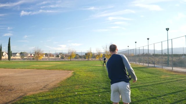Two young men playing catch and having fun during team practice with a baseball and glove in a grassy park field SLOW MOTION.