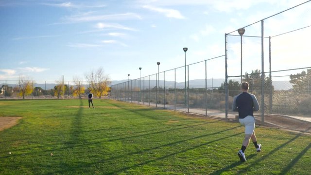 A baseball player sprinting to make an athletic catch then jumping and throwing the ball to his team mate in the outfield in slow motion.