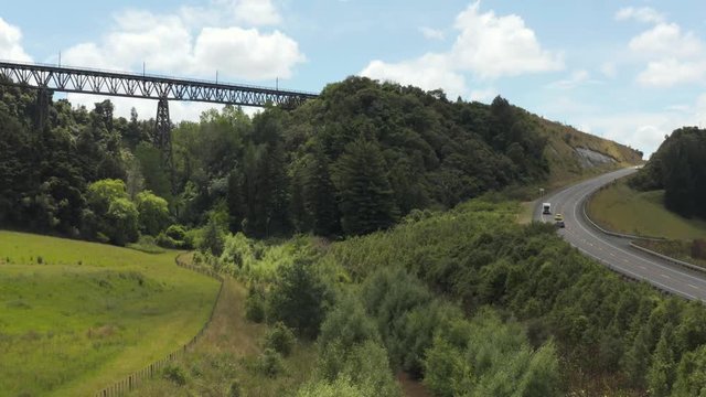 Low angle aerial of state highway one with holiday traffic going past rangitikei region with railway bridge. 4k