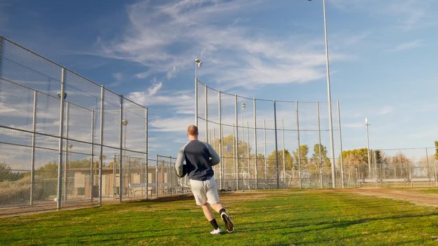 A young man playing catch on a baseball diamond throwing a ball to a team mate in the park under blue skies SLOW MOTION.