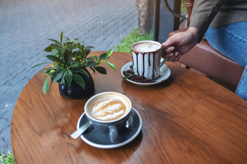 Closeup image of a hand holding a cup of hot chocolate with another cup of coffee on wooden table in cafe