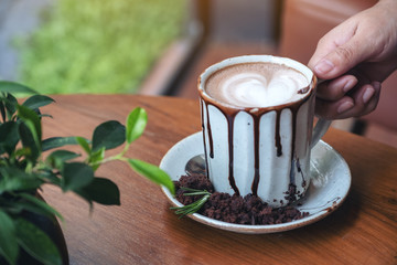 Closeup image of a hand holding a cup of hot chocolate on wooden table in cafe