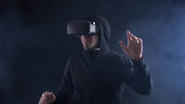 Man getting experience in using VR-headset on dark smoky background. Augmented reality device creating virtual space.