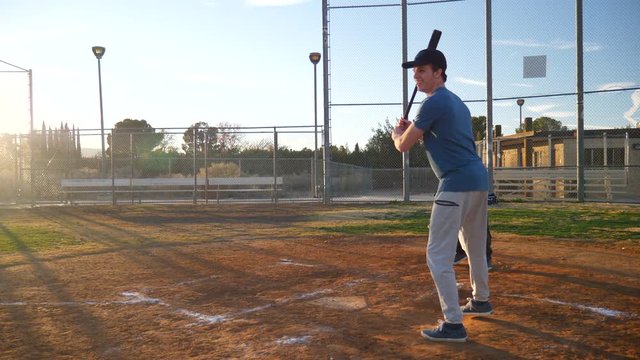 A young man baseball player makes a hit with his bat and runs to first base with friends in a park at sunset SLOW MOTION.